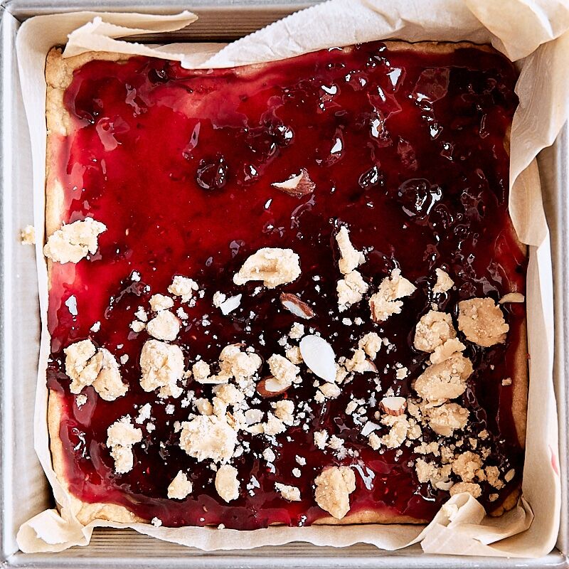 Crumb topping sprinkled over jam layer of crumb bars