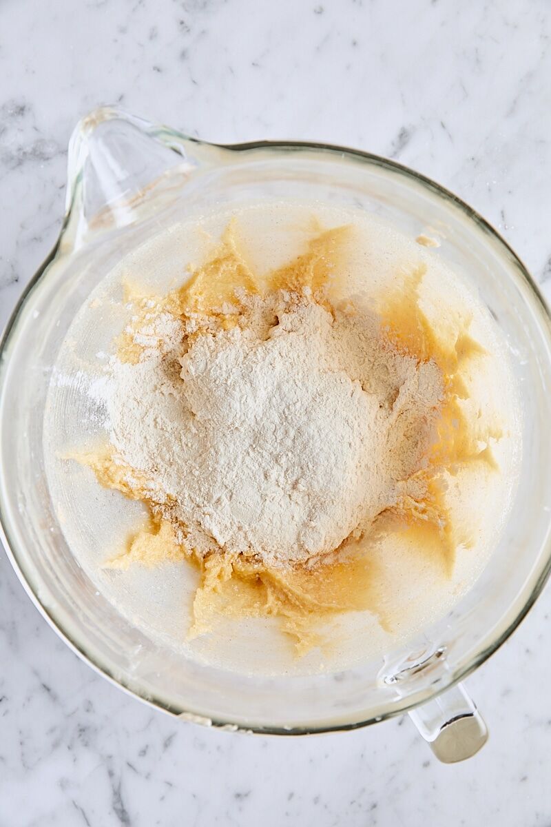 Flour mixture added to sugar cookie dough in glass mixing bowl