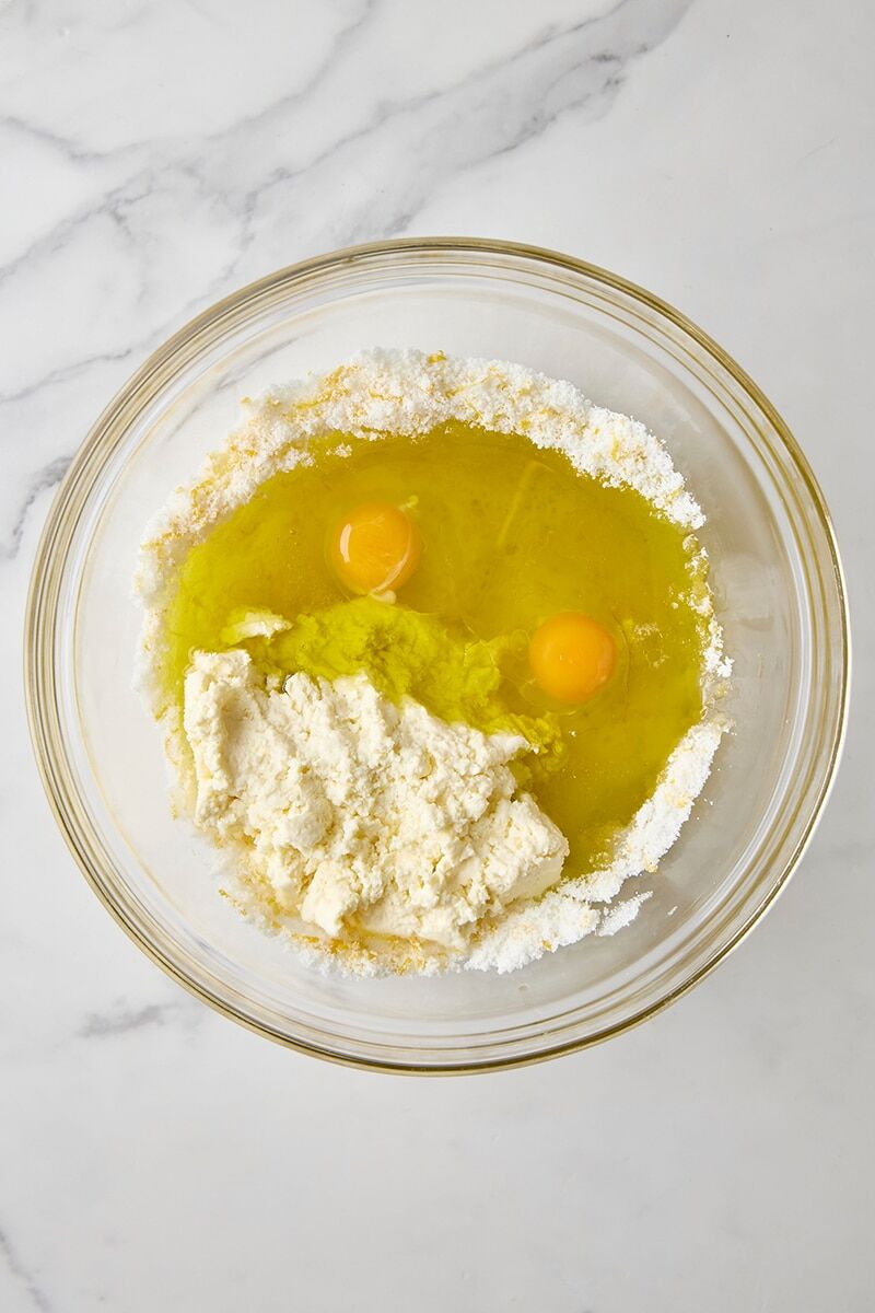 Lemon olive oil, ricotta, eggs, lemon juice, and lemon-sugar in glass bowl
