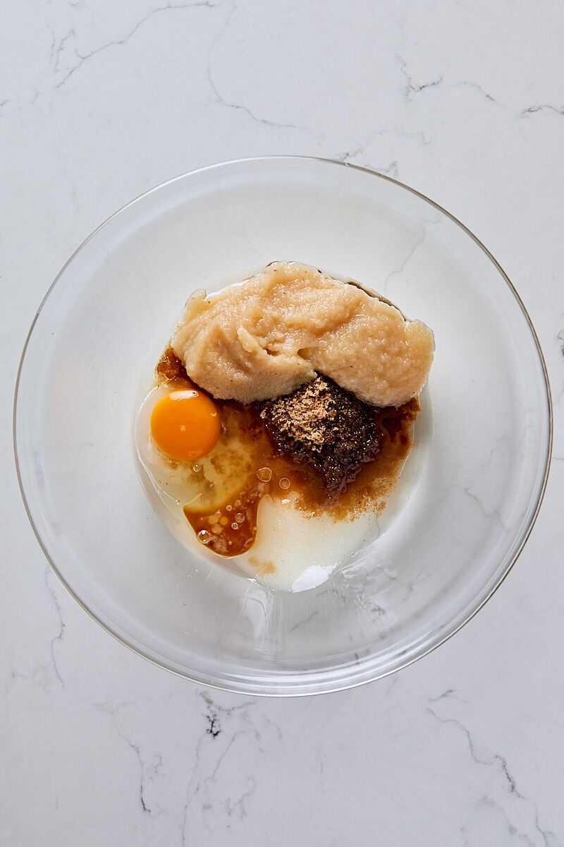 Unsweetened applesauce, baking oil, sugar, dark brown sugar, egg, vanilla, and lemon juice in medium glass bowl