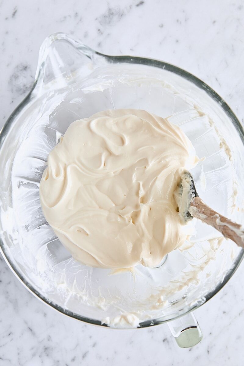 Sour cream and vanilla mixed into cheesecake batter in glass mixing bowl