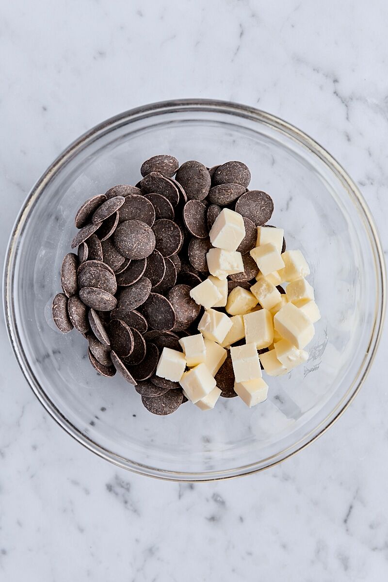 Semisweet chocolate wafers and cubed unsalted butter in glass bowl