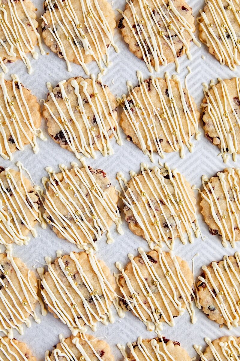 Cranberry orange shortbread drizzled with white chocolate on parchment-lined baking sheet