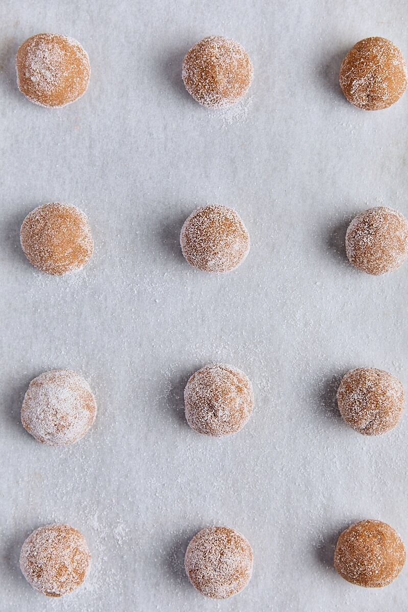 Molasses cookie dough scooped into balls and rolled in sugar on parchment-lined baking sheet