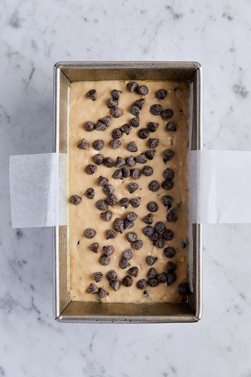 Chocolate chips sprinkled over banana bread batter in parchment-lined loaf pan