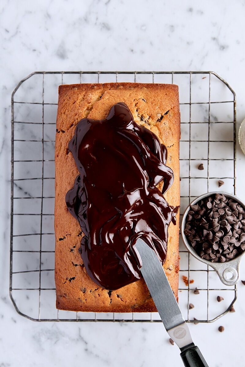 Baked chocolate chip loaf cake on wire cooling rack topped with chocolate ganache
