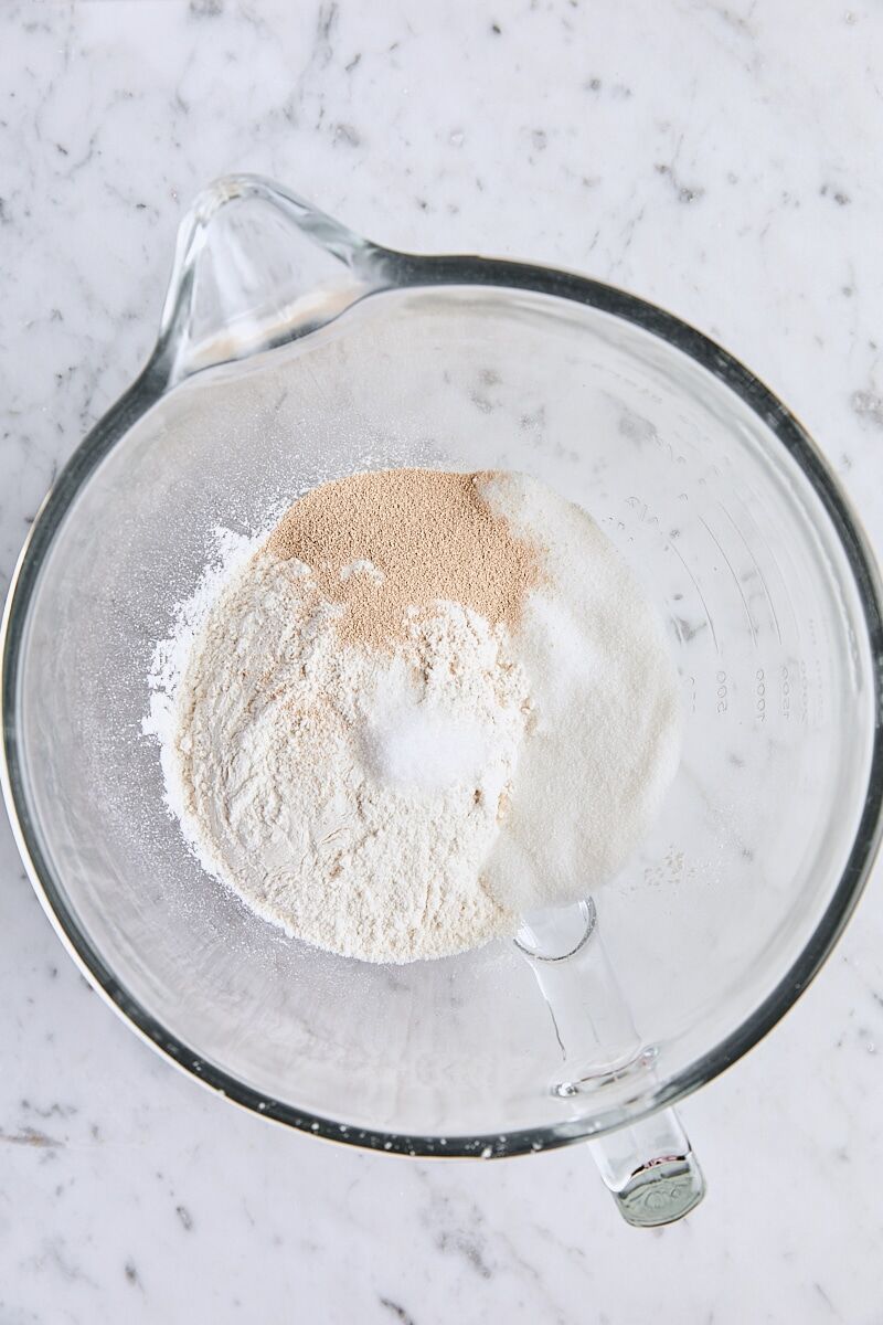 Flour, instant yeast, granulated sugar, and salt in glass mixing bowl