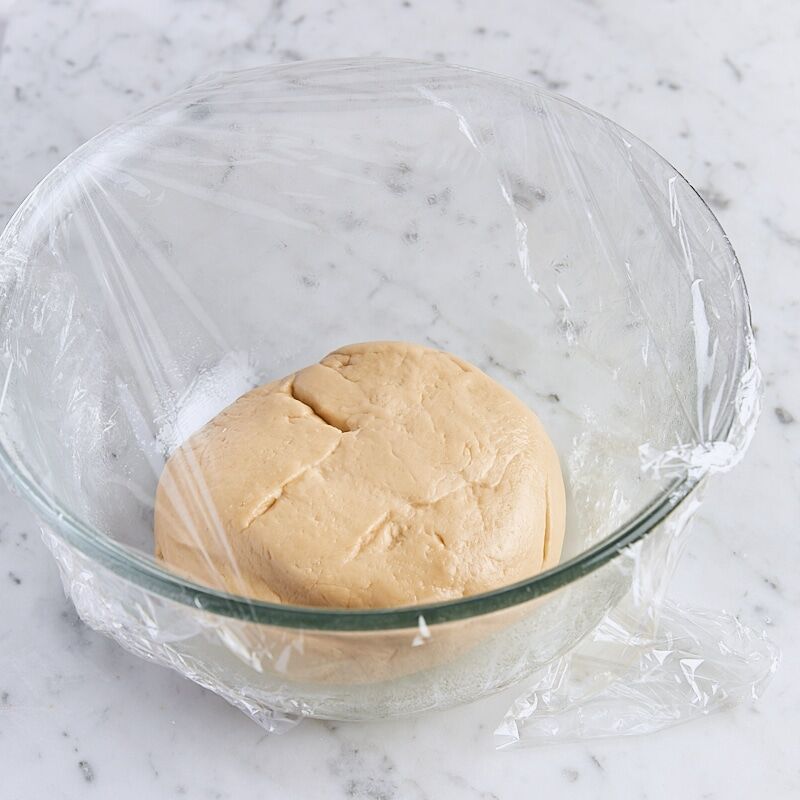 Dough in glass mixing bowl covered with plastic wrap, pre-rise