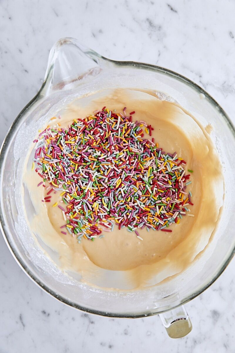 Rainbow sprinkles added to batter in glass mixing bowl