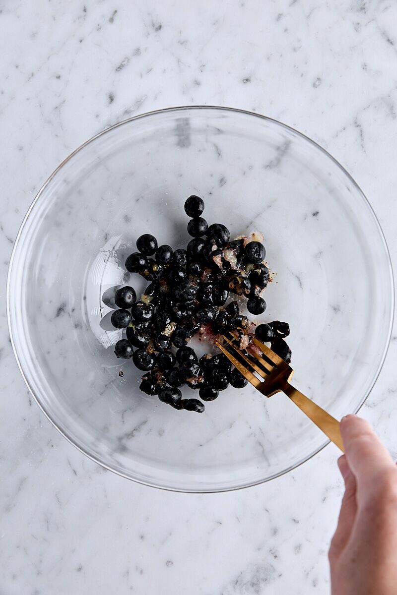 Crushed fresh blueberries in glass bowl with fork.