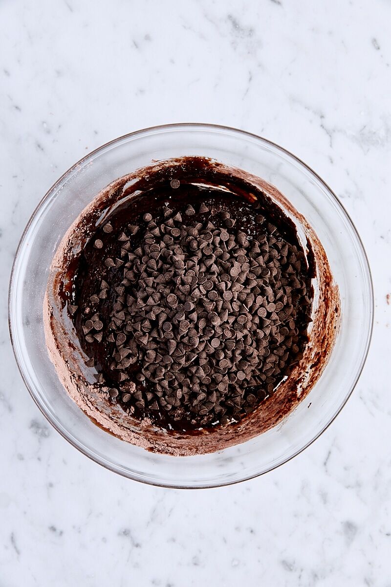 Chocolate chips added to brownie batter in glass bowl