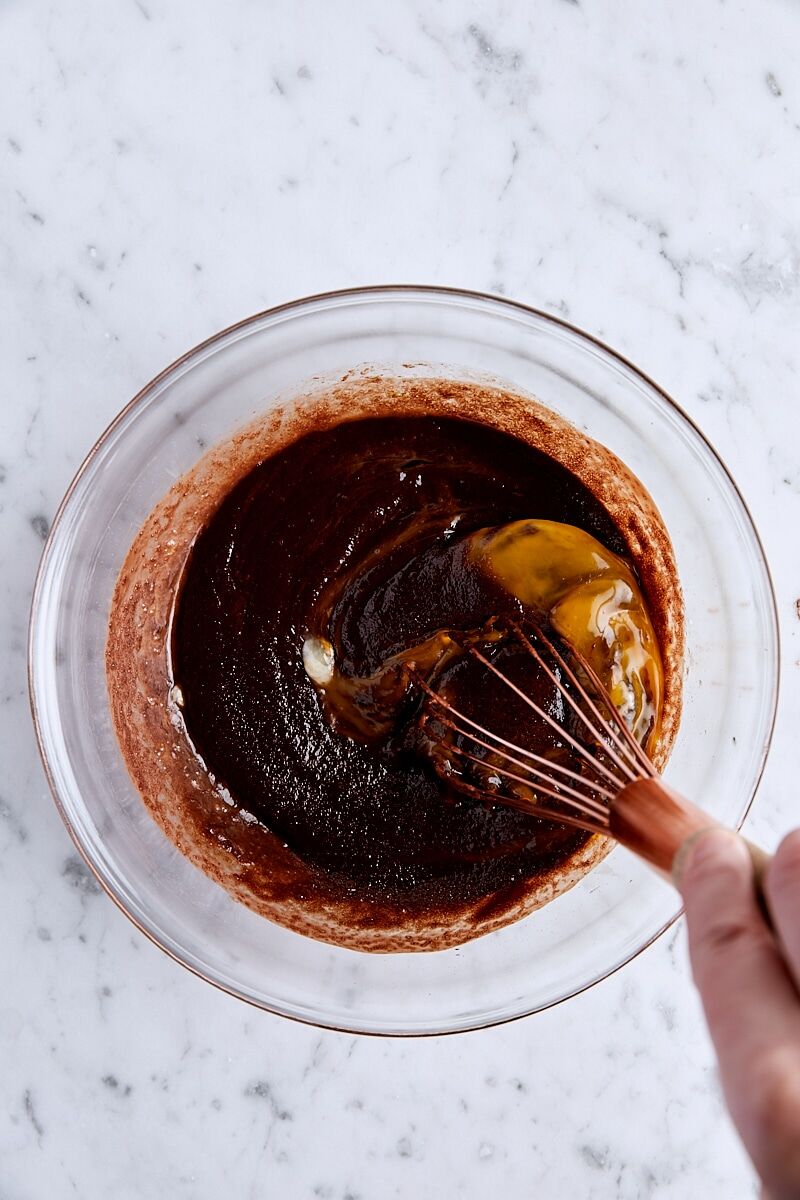 Eggs whisked into melted chocolate mixture in glass bowl