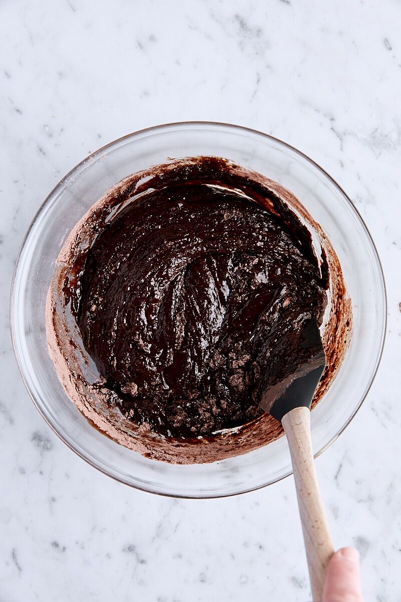 Flour mixture folded into brownie batter in glass bowl