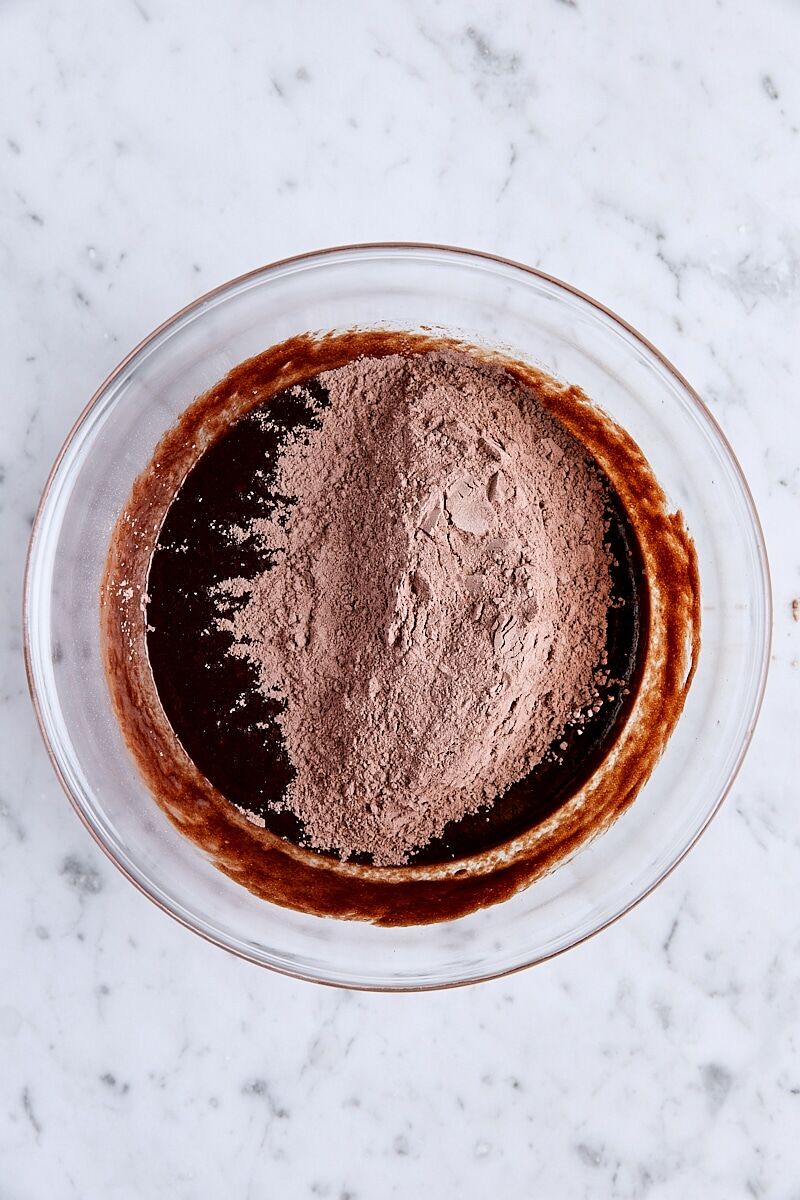 Flour mixture added to brownie batter in glass bowl