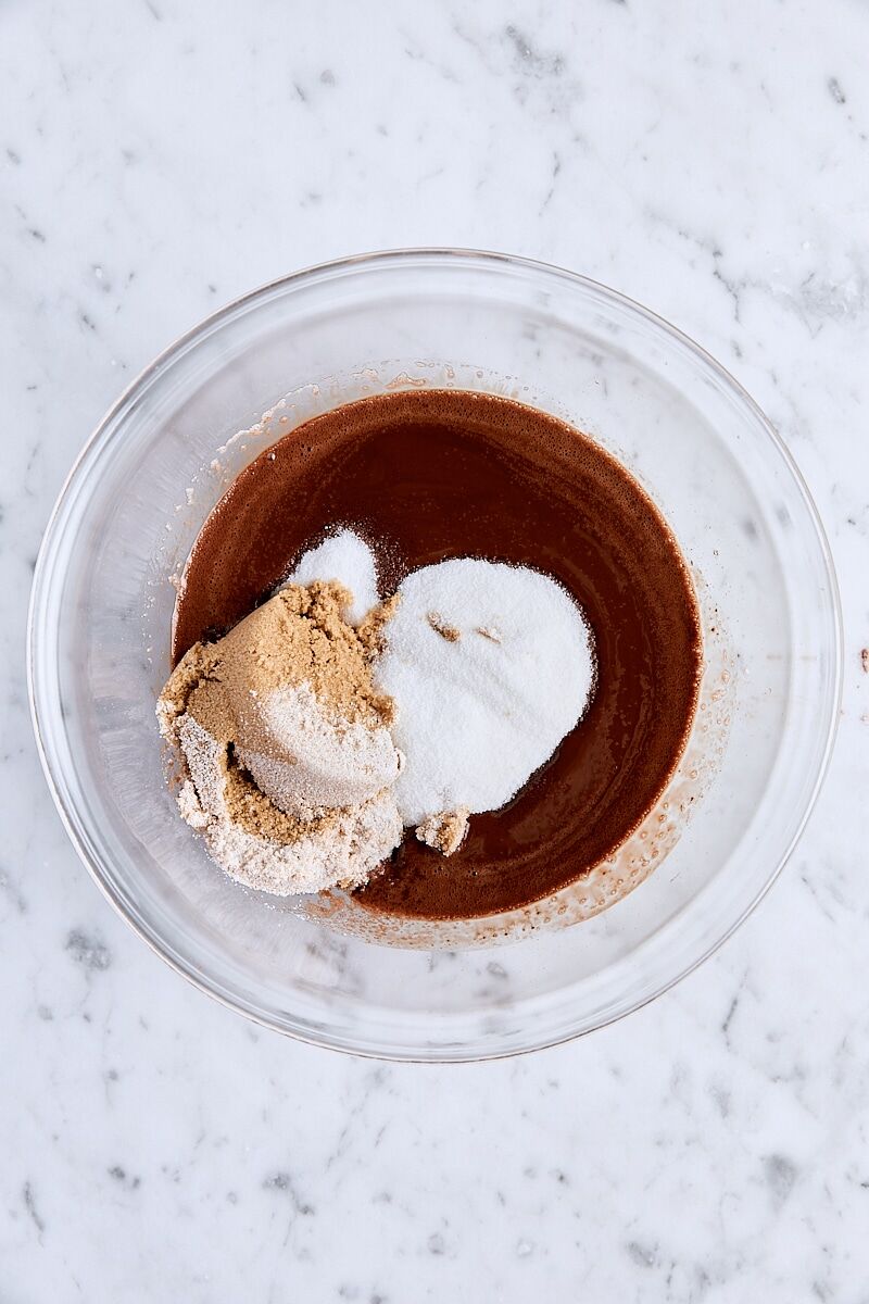 Granulated sugar and light brown sugar added to glass bowl with melted chocolate mixture