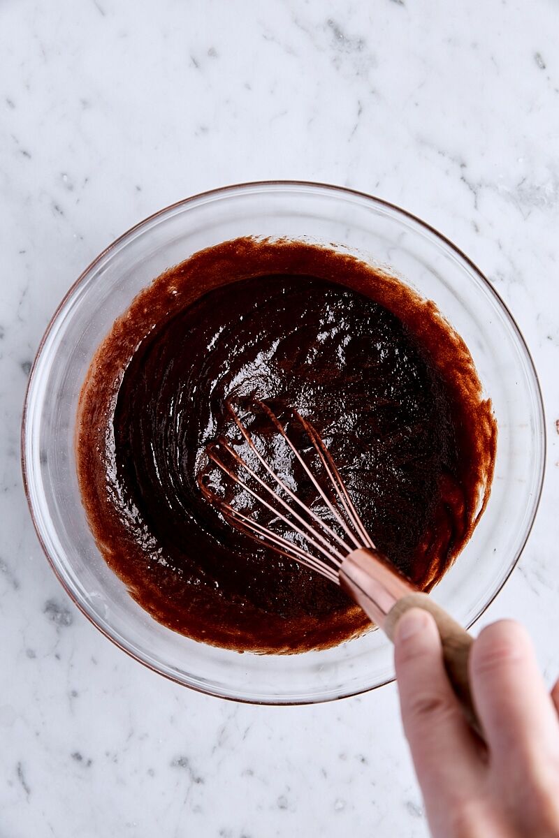 Vanilla extract whisked into melted chocolate mixture in glass bowl