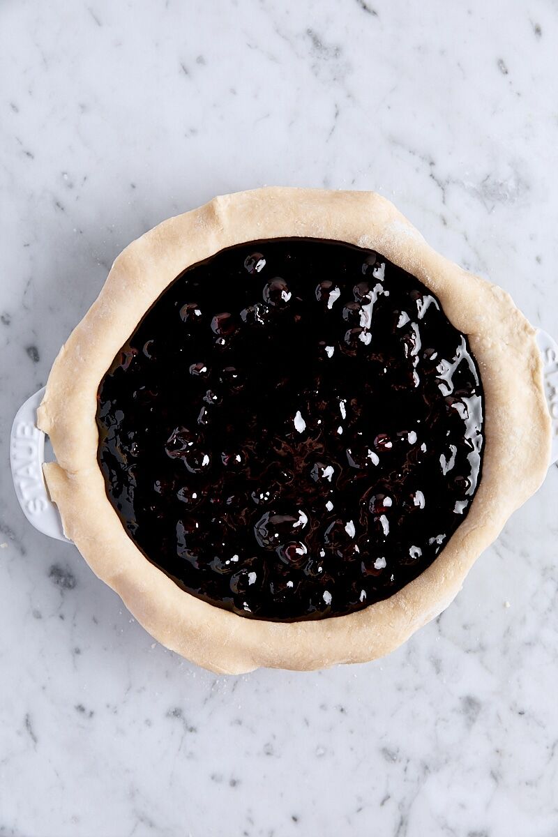 Blueberry filling spooned into pie dough in pie pan