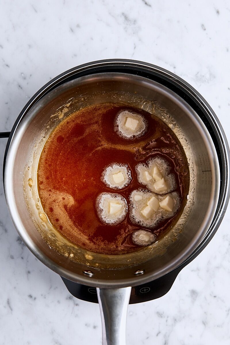 Cubed butter added to caramel mixture in light-colored saucepan