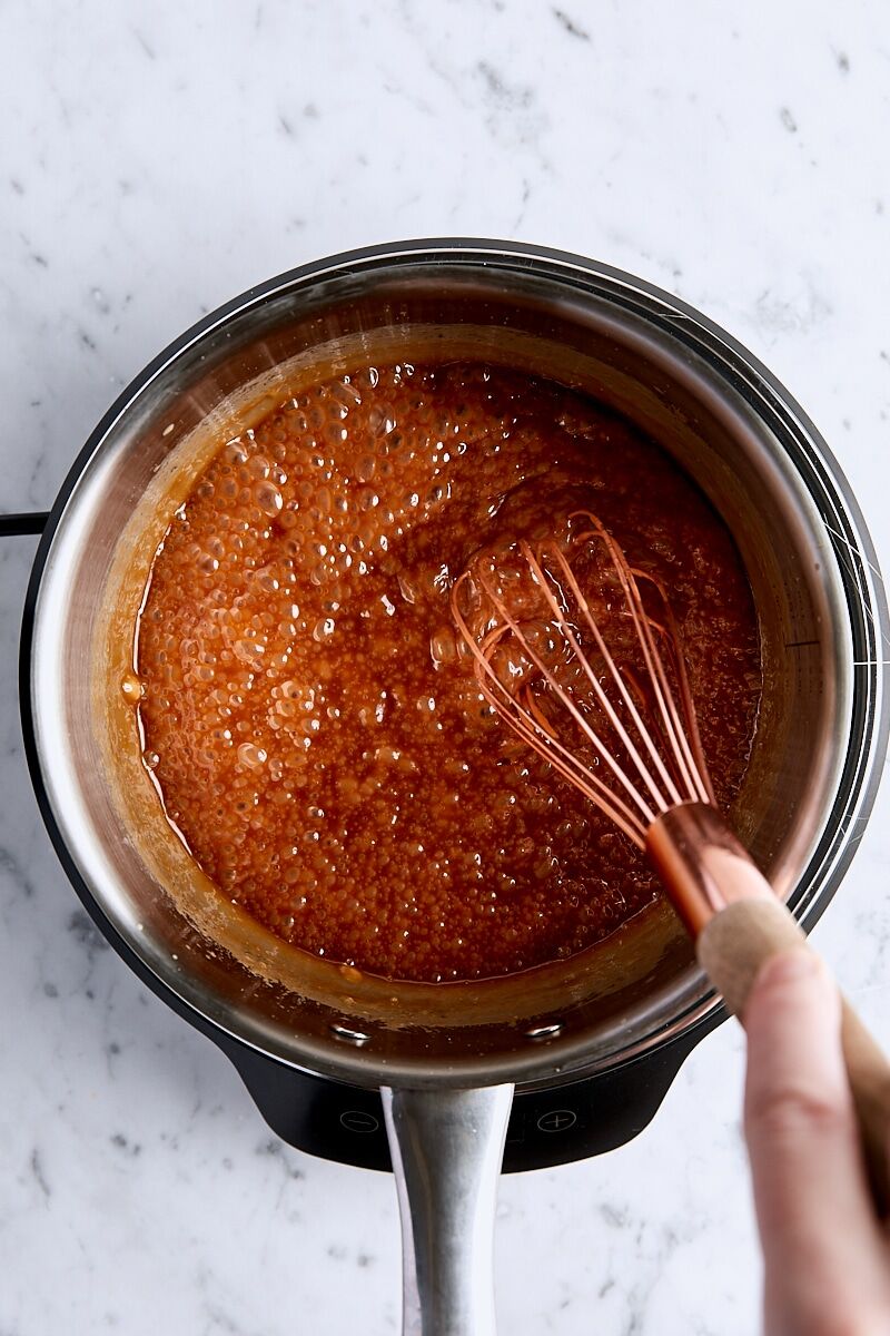Cream whisked into caramel mixture in light-colored saucepan