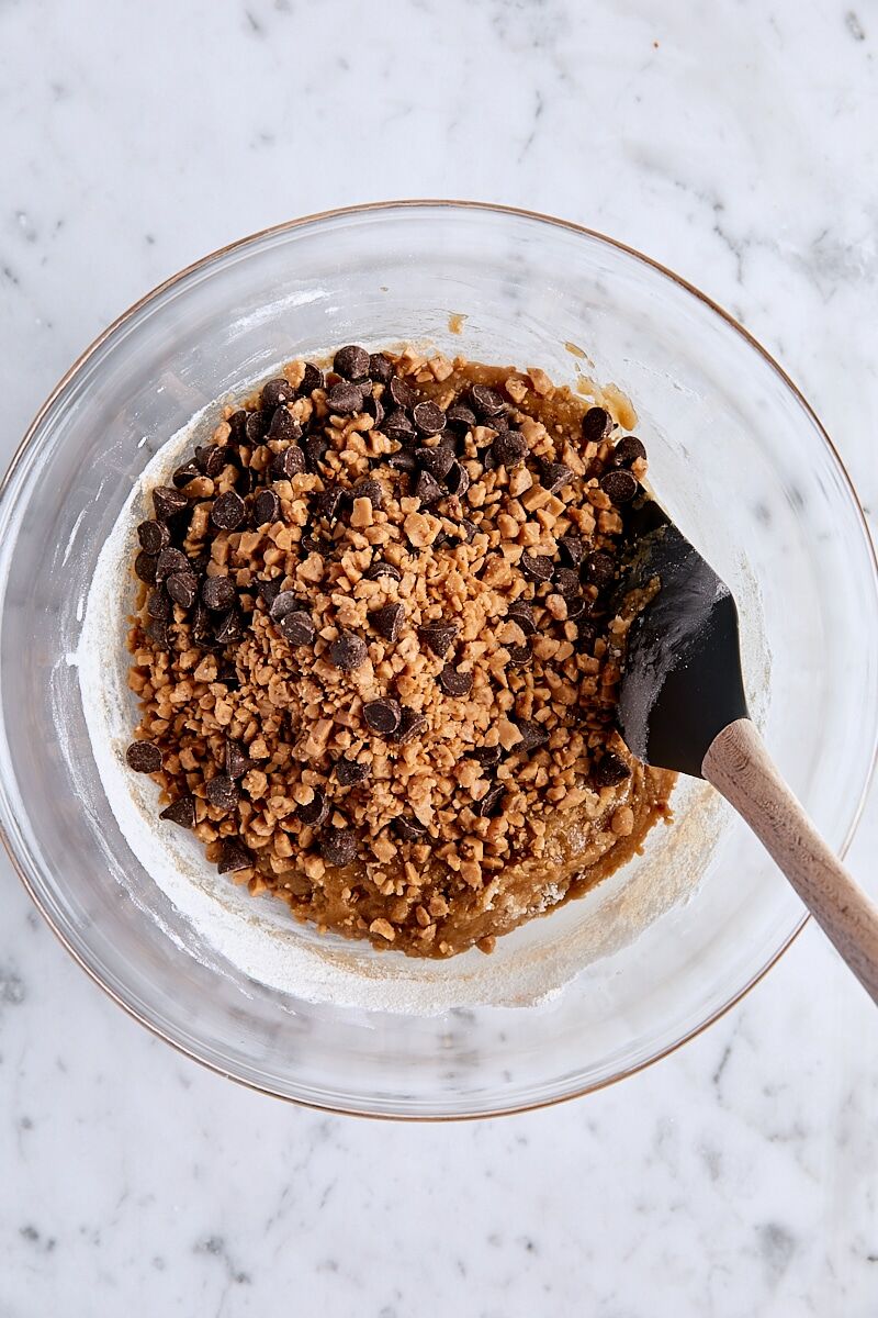 Toffee bits and chocolate chips added to blondie batter in glass bowl