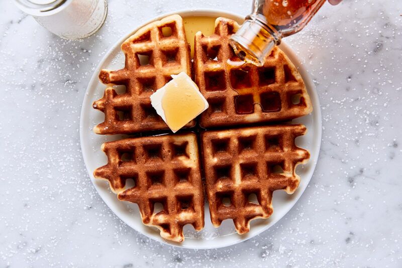 Belgian-style yeast waffle on white plate topped with butter and maple syrup