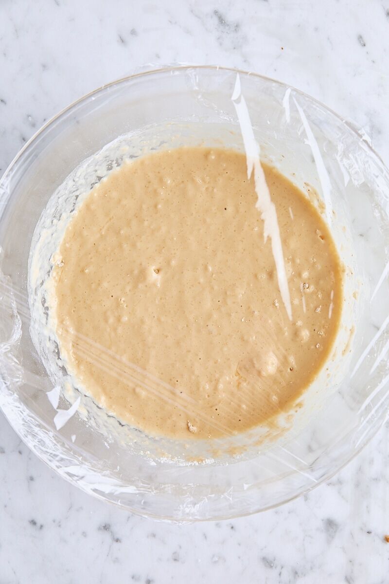 Waffle batter in large glass bowl covered with plastic wrap