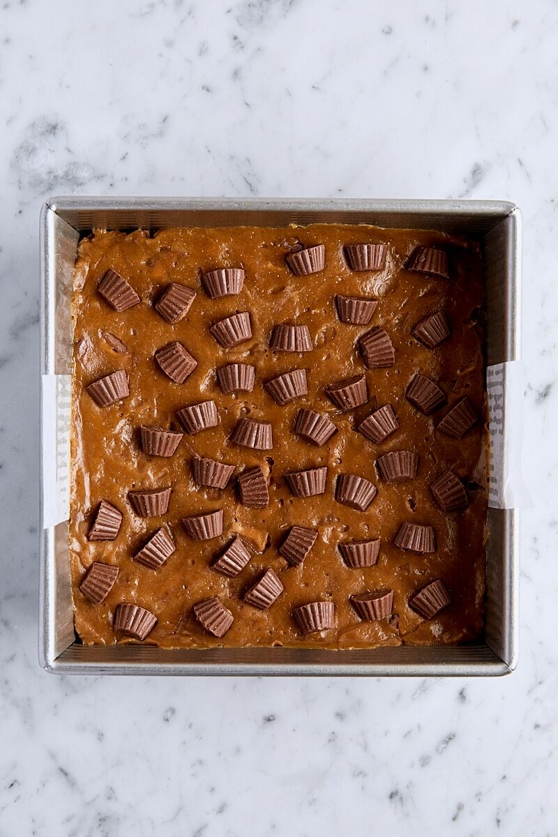 Peanut butter blondie batter topped with mini peanut butter cups in parchment-lined square pan