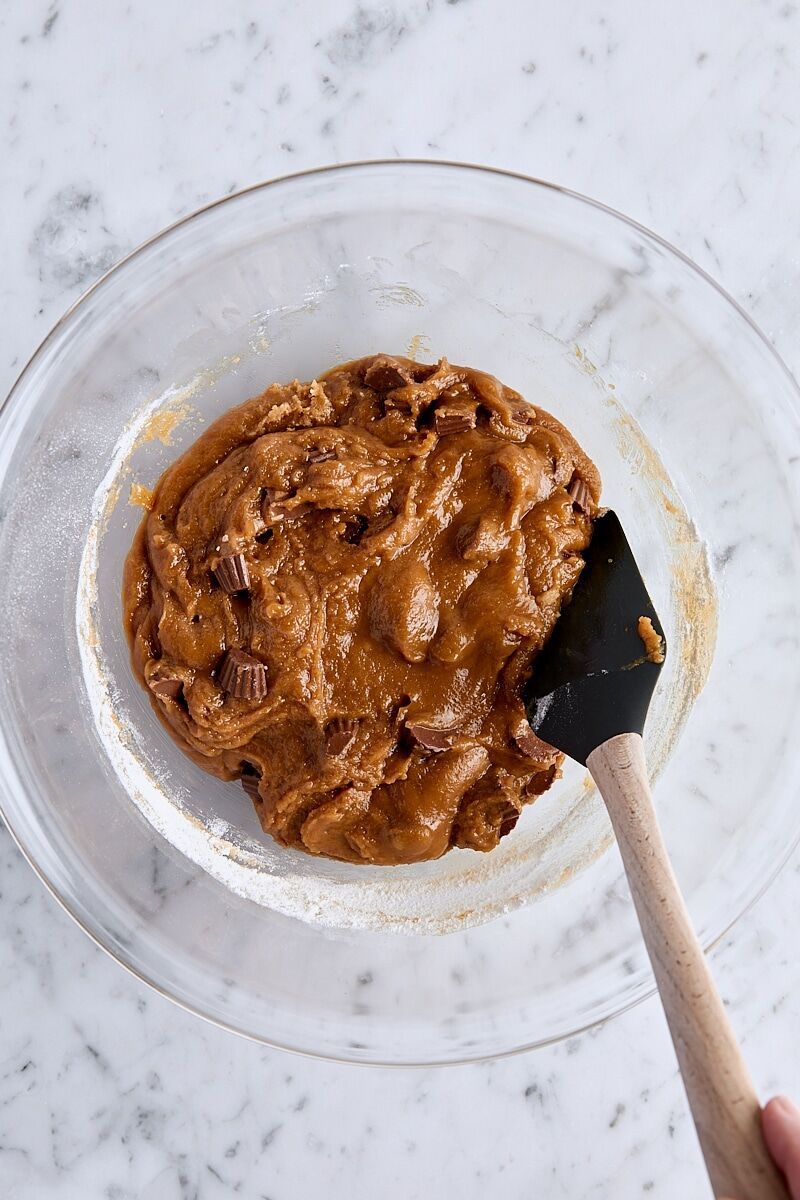 Mixed peanut butter cup blondie batter in glass bowl with spatula