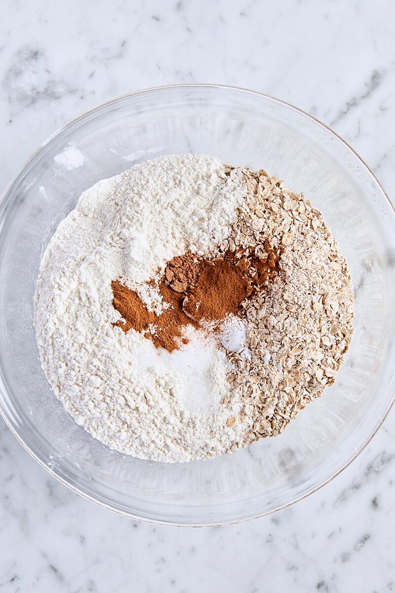 Coarsely ground oats, flour, baking powder, baking soda, cornstarch, salt, cinnamon, and nutmeg in glass bowl