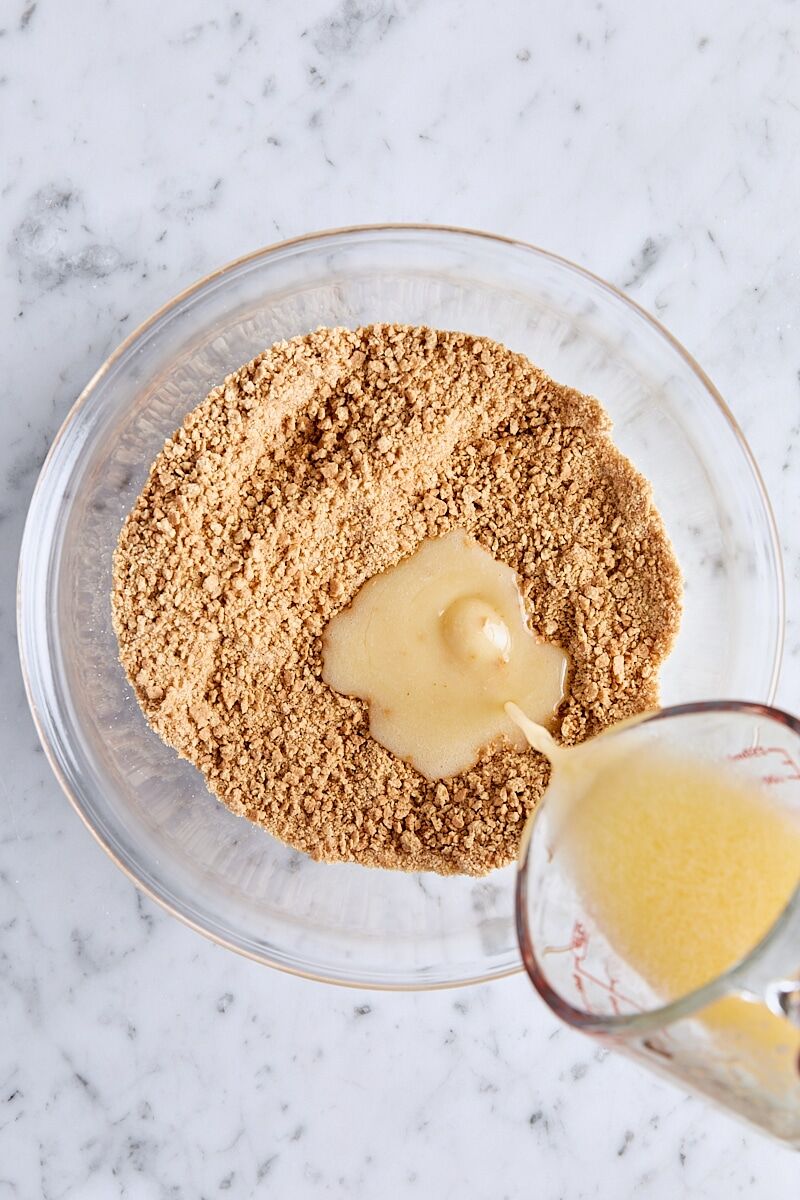 Melted butter added to graham cracker mixture in glass bowl