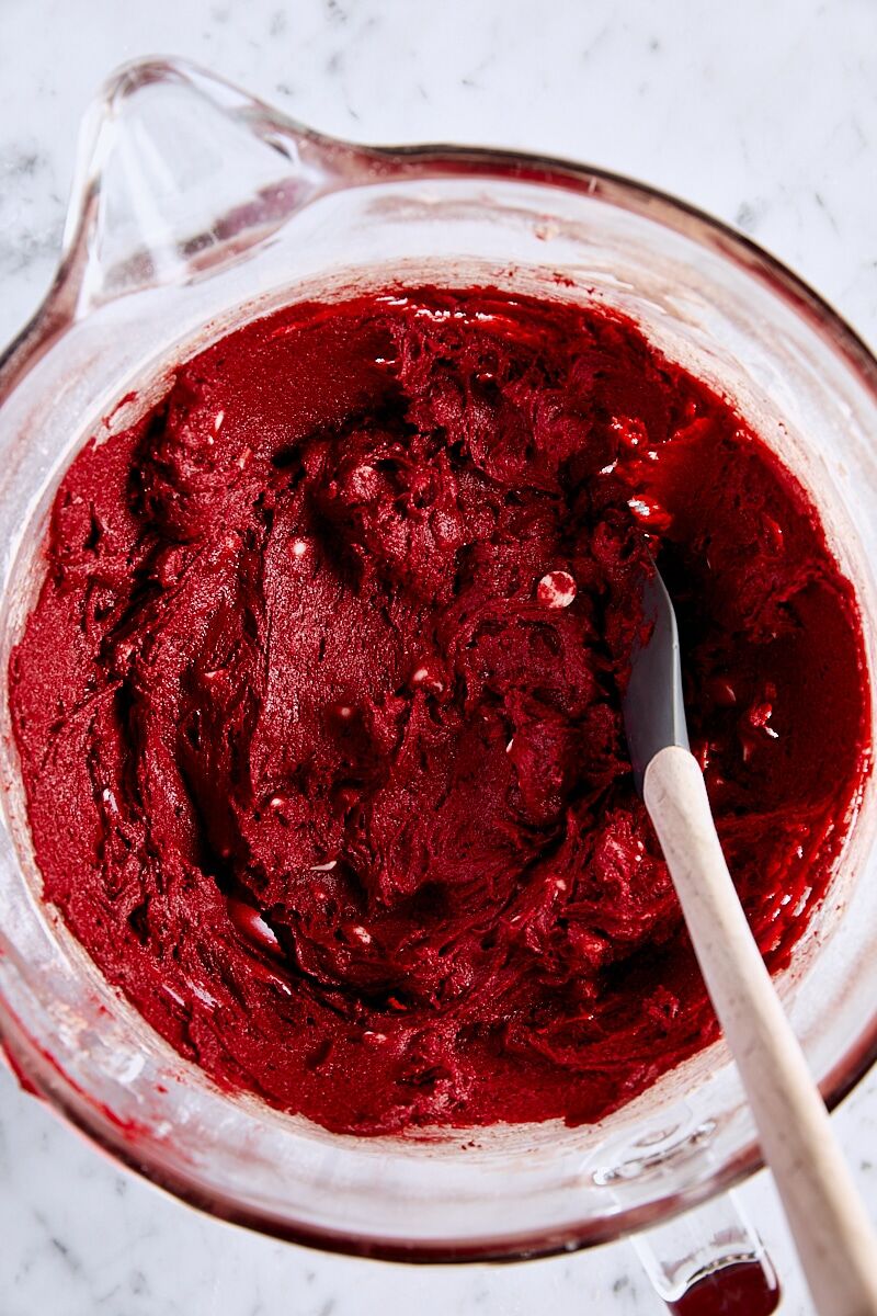 Red velvet cookie dough in glass mixing bowl with spatula