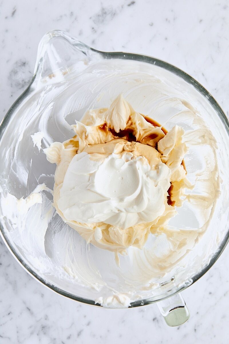 Sour cream and vanilla extract added to cheesecake batter in glass mixing bowl