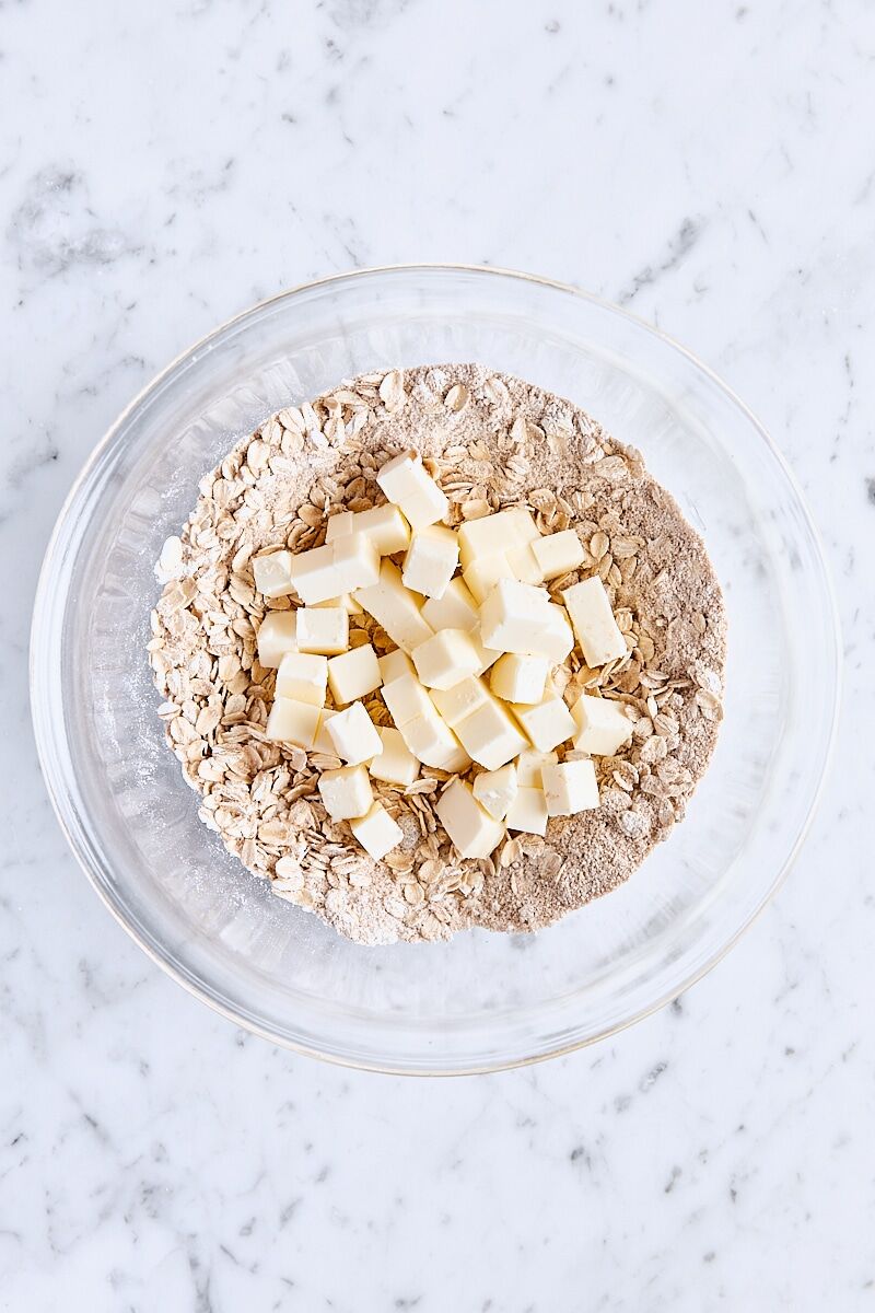Cubed butter added to oatmeal mixture in glass bowl