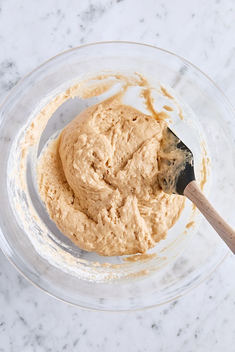Mixed apple fritter bread batter in large glass bowl with spatula