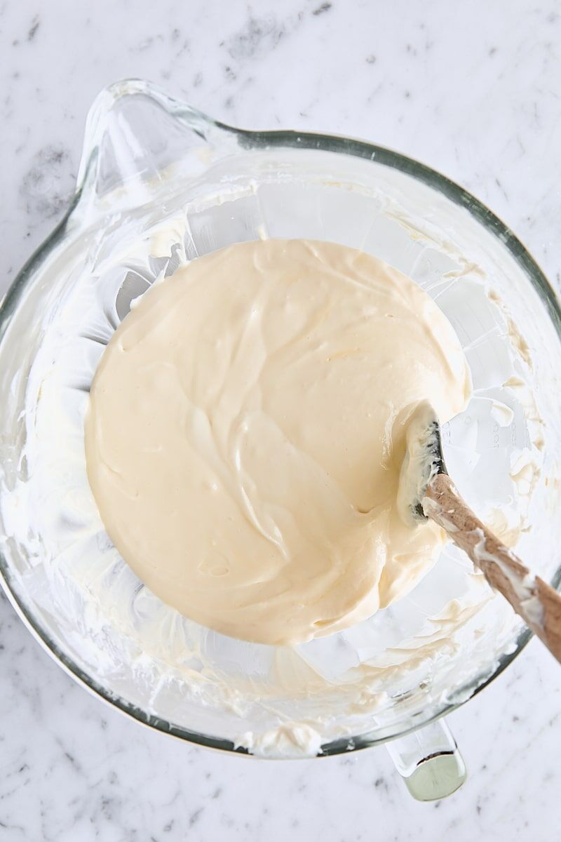 Egg mixed into cheesecake batter in glass mixing bowl