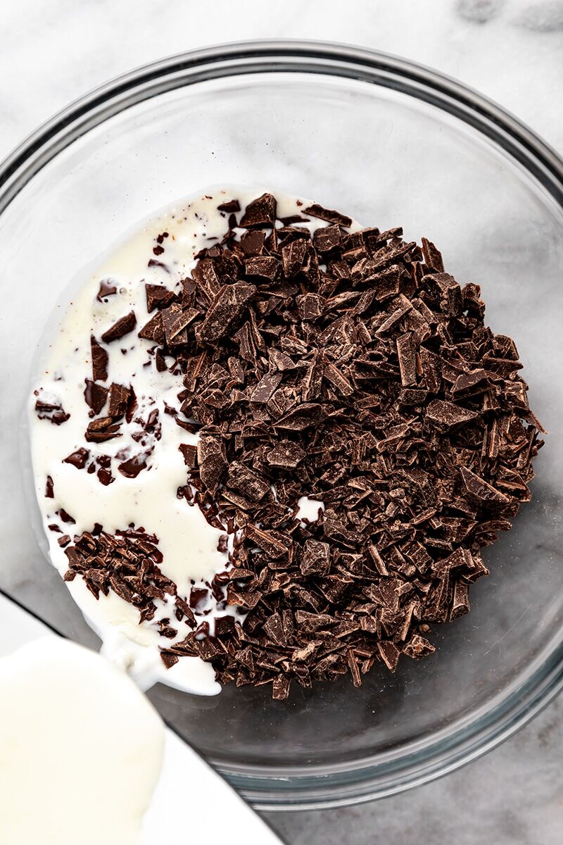Warm heavy cream poured over chopped chocolate in glass bowl