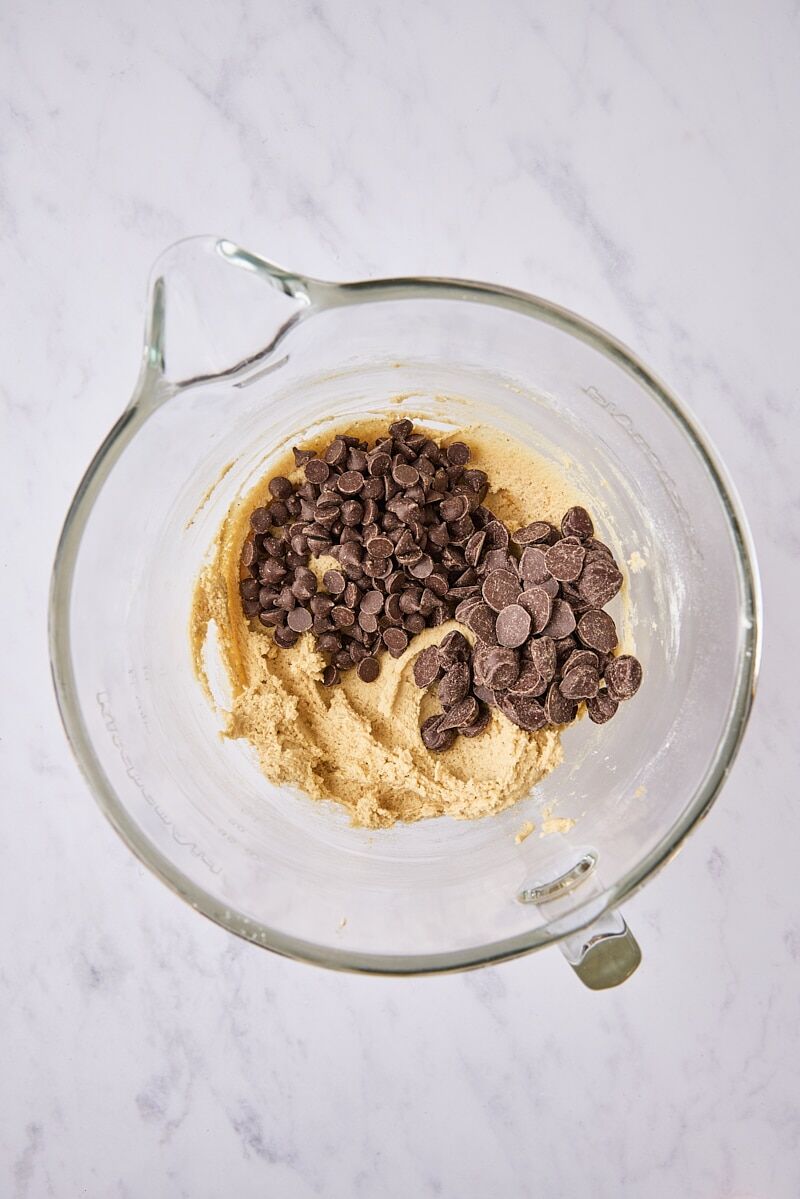 Chocolate chips added to cookie dough in glass mixer bowl