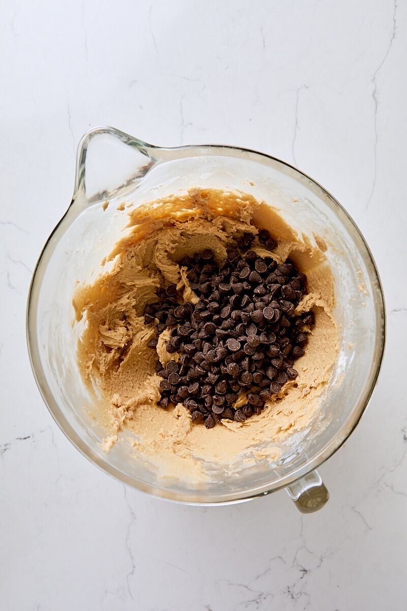 Chocolate chips added to cookie dough in glass mixer bowl