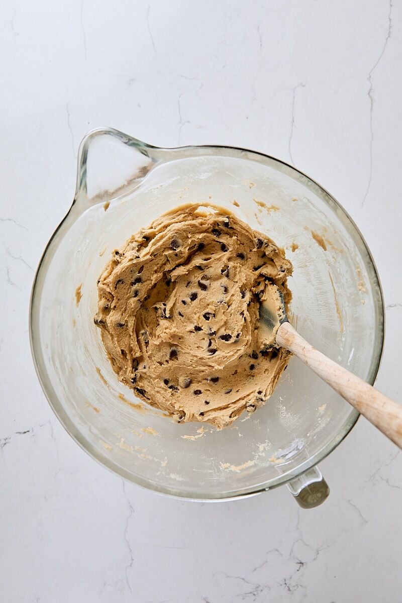Chocolate chip dough in glass mixer bowl with spatula