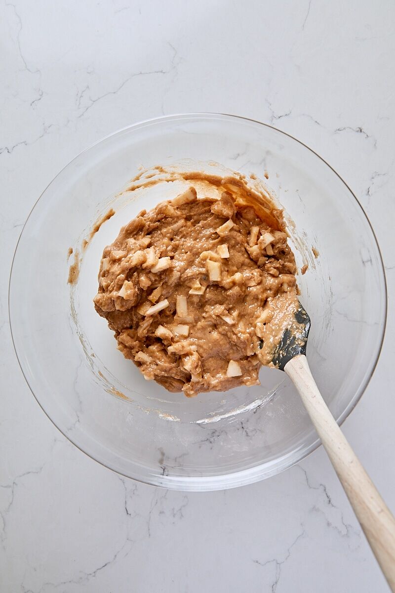 Mixed apple cinnamon muffin batter in glass bowl with spatula