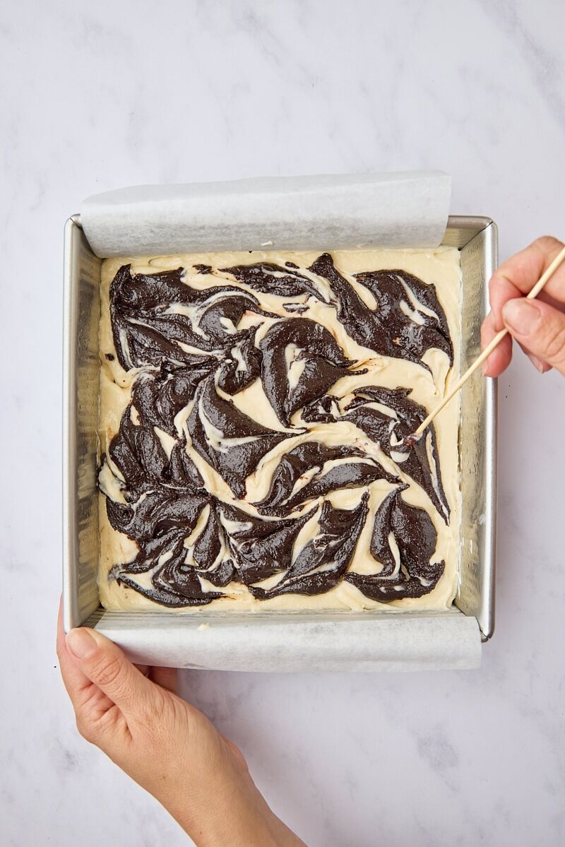 Dollops of brownie batter swirled into cream cheese layer with wooden skewer