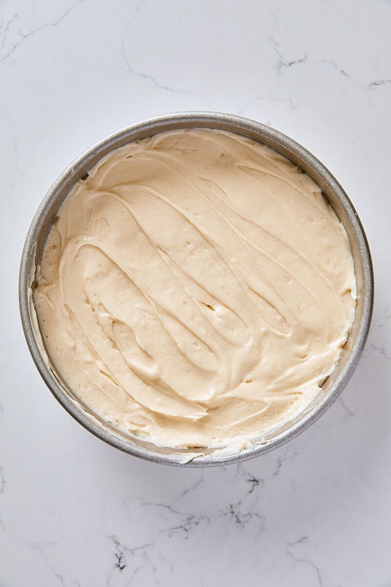 Cake batter layered over peach slices in round cake pan