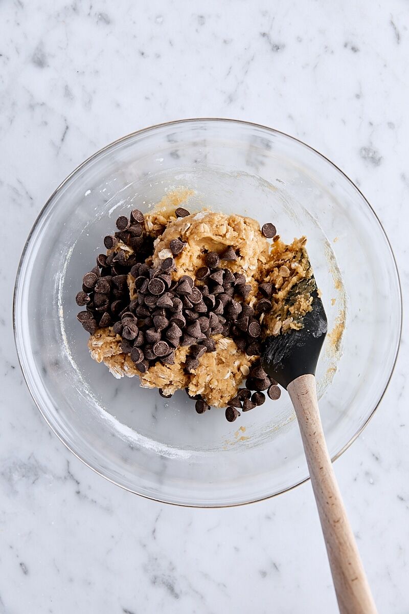 Chocolate chips added to dough in a glass bowl with spatula