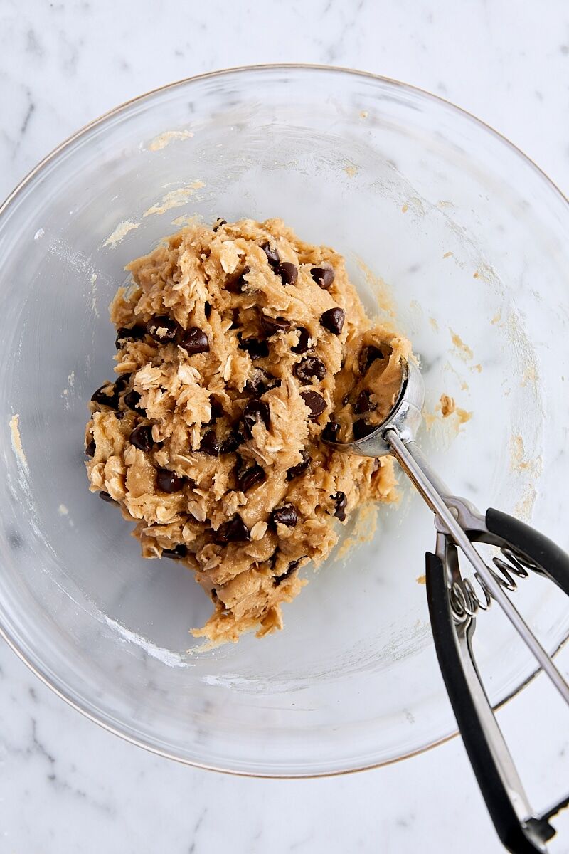 Mixed oatmeal chocolate chip cookie dough in glass bowl with cookie scoop
