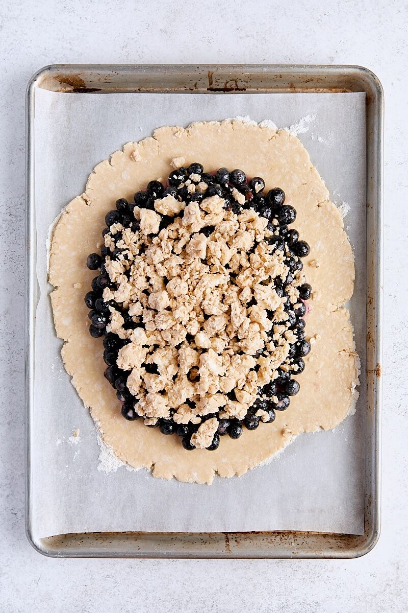 Pie dough topped with blueberry filling and crumble topping on parchment-lined baking sheet
