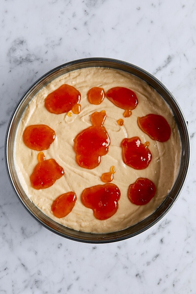 Cake batter topped with spoonfuls of jam in springform pan