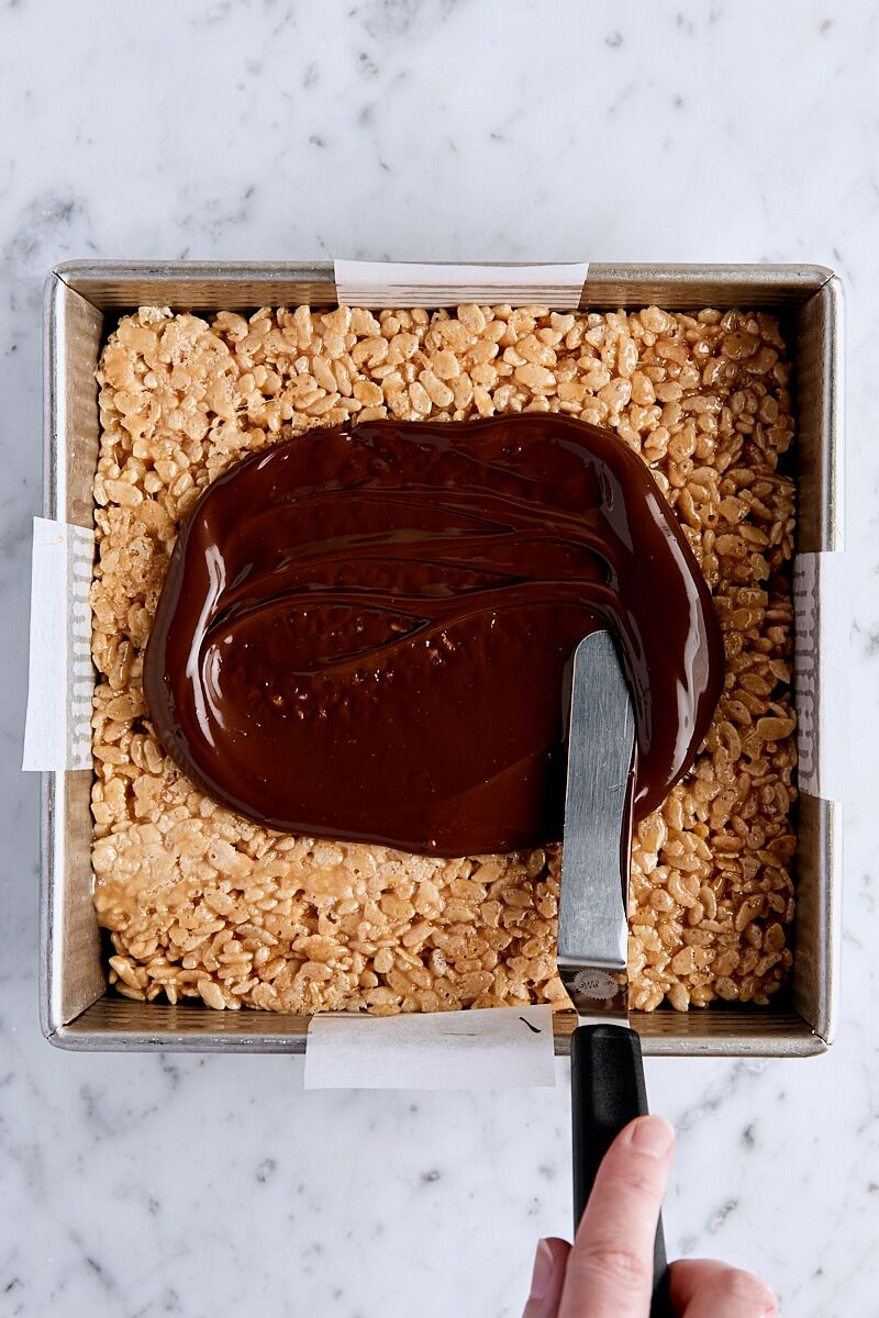 Melted chocolate spread over rice krispie mixture with offset spatula