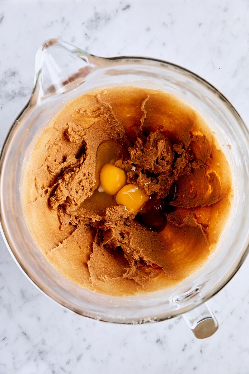 Egg, egg yolk, and vanilla added to ginger cookie dough in glass mixing bowl