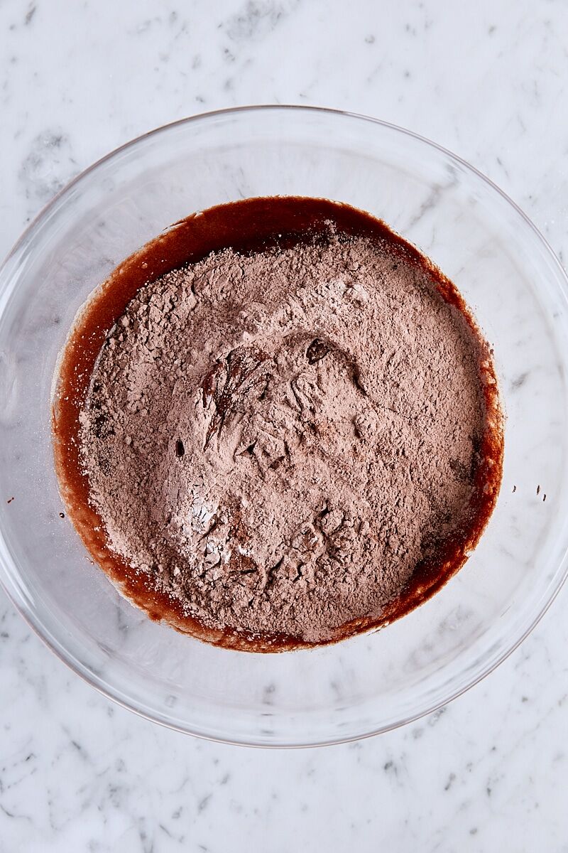 Flour mixture added to large glass bowl with chocolate mixture