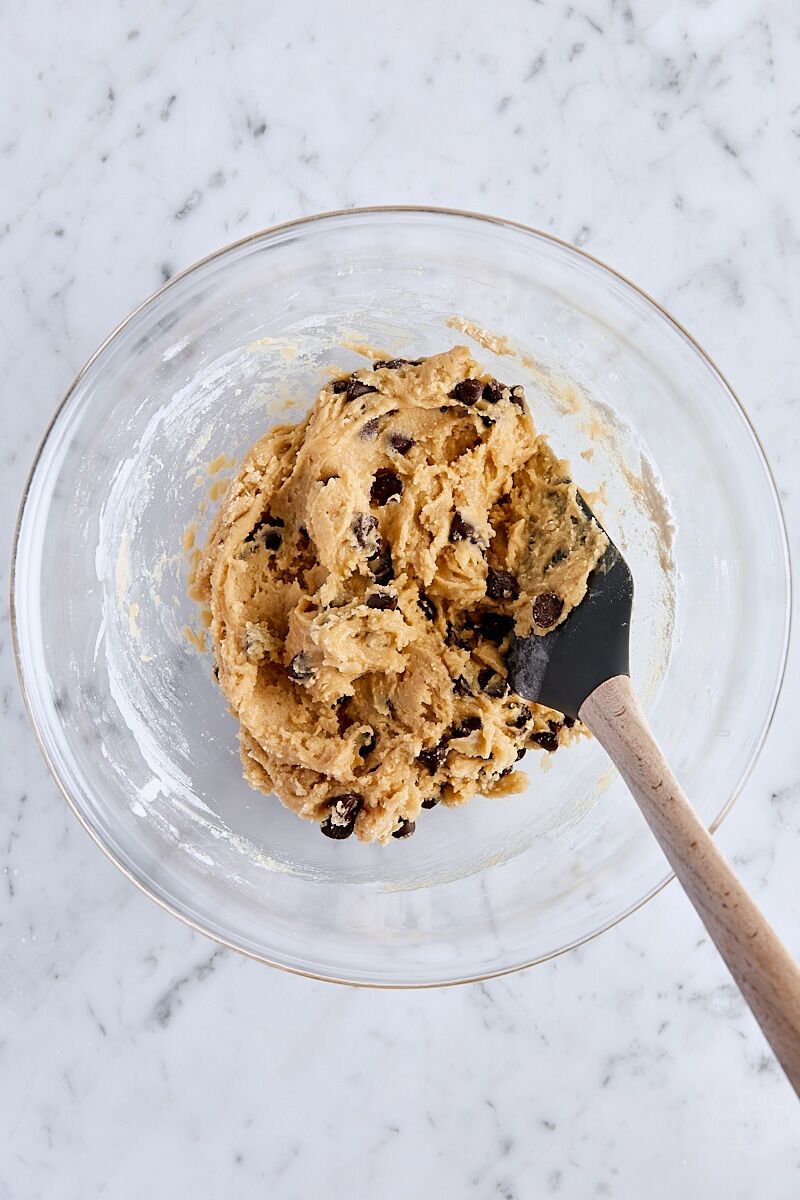 Mixed chocolate chip cookie dough in glass bowl with spatula